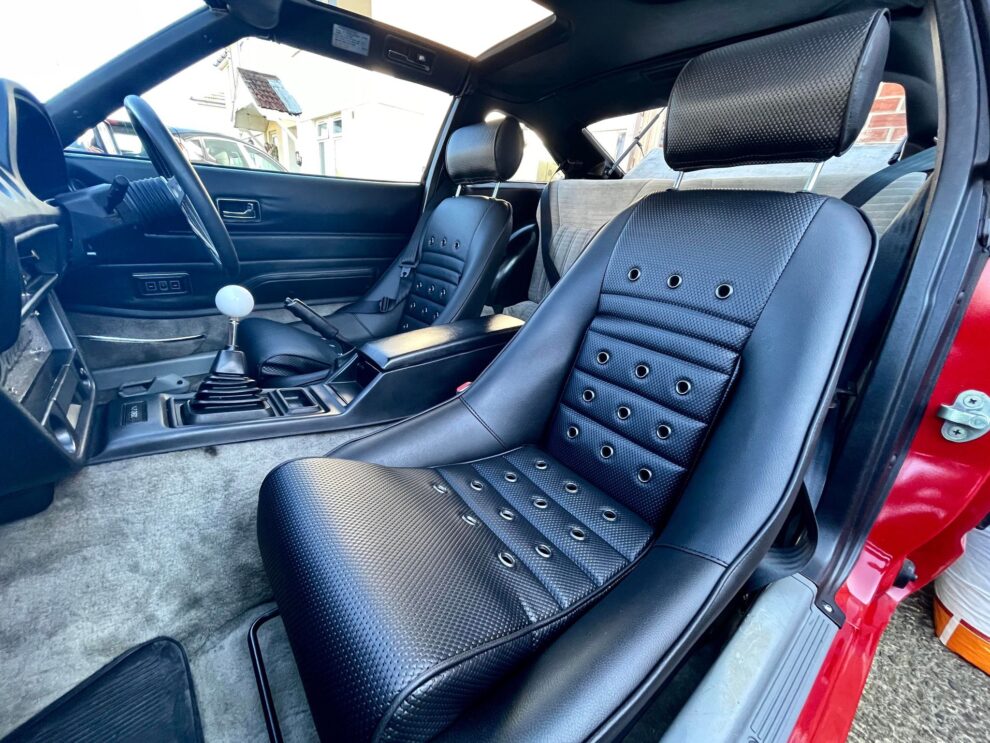 A black Cobra GT3 Historic bucket seat with eyelets and headrest fitted in a customer's Datsun, seen through the open door
