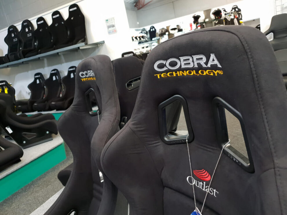 Close view of the embroidered Cobra Technology logo on the head restraint of a black bucket seat, with more seats behind