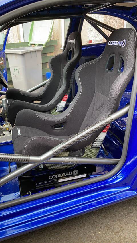 Two black Corbeau Pro Series X bucket seats on black Corbeau frames inside a blue caged Seat Ibiza, seen through the passenger door