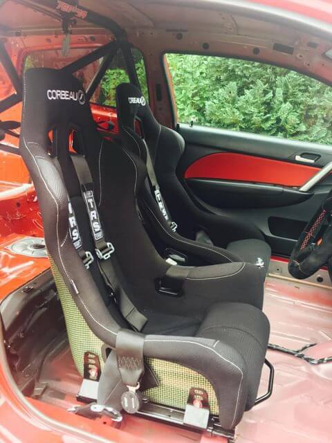 Two black Corbeau Pro Series X bucket seats with black TRS harnesses fitted in a stripped red Honda Civic EP3 with a roll cage