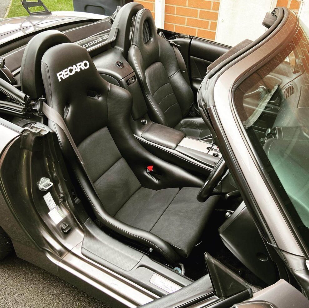A black Recaro Pole Position bucket seat with suede centre fitted in the driver's side of a grey Honda S2000 with the roof down