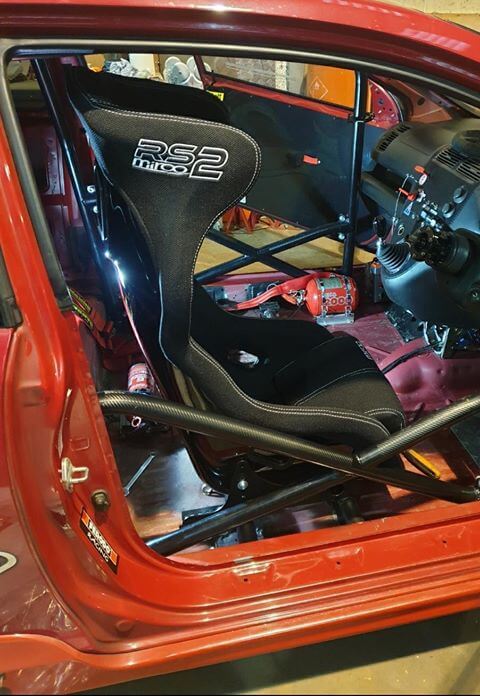 A black Mirco RS2 bucket seat seen through the open driver door of a red Honda Civic, with the black roll cage around it