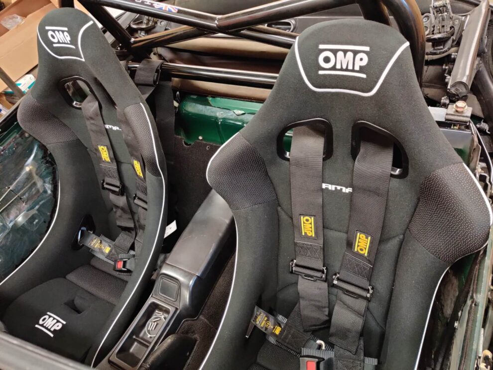 Two black OMP bucket seats with black OMP harnesses fitted in a Mazda MX-5 with a roll cage