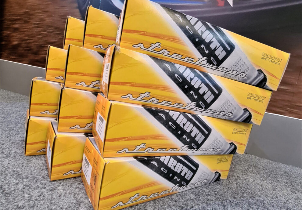 Stacked yellow boxes of Schroth Racing streetwear harnesses marked Schroth Safety Products on the carpet of the showroom