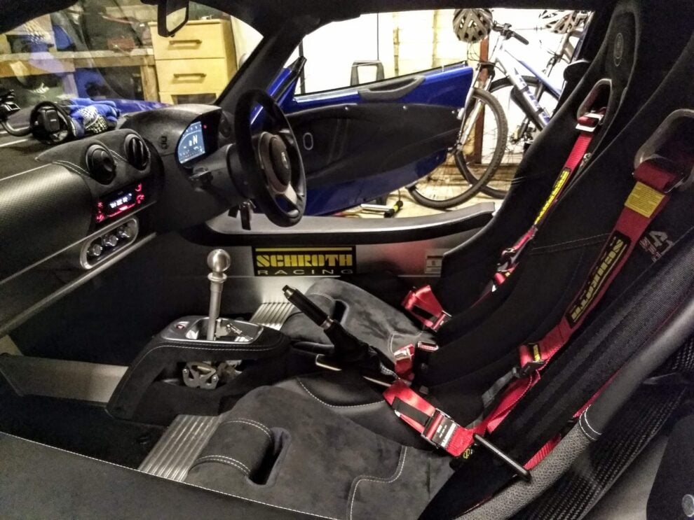 The passenger side of a Lotus Exige interior with a red Schroth harness on the seat and the Schroth Racing sticker on the sill