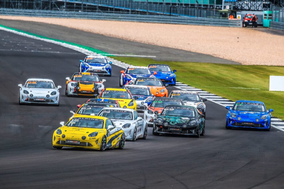 A field of Alpine A110 race cars in different liveries on track at a circuit