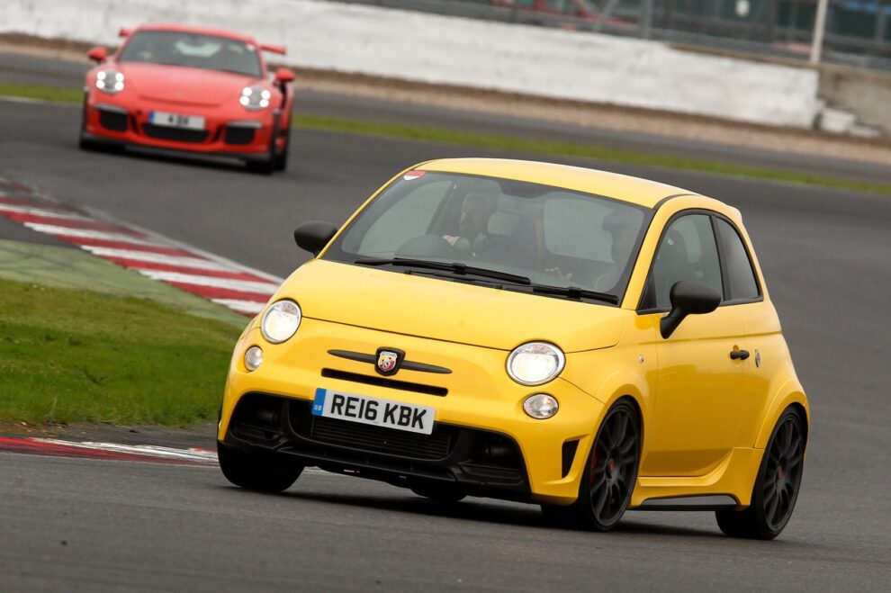A yellow Abarth 595 cornering on a race circuit with an orange Porsche following behind