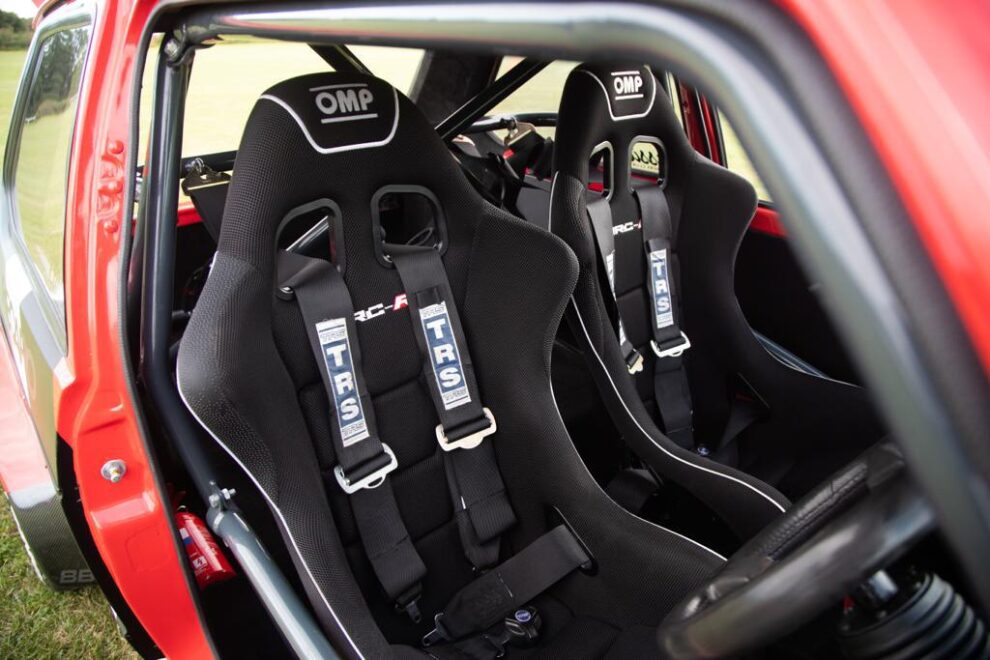 Two black OMP WRC-R bucket seats with black TRS harnesses inside a red VW Golf with a grey roll cage