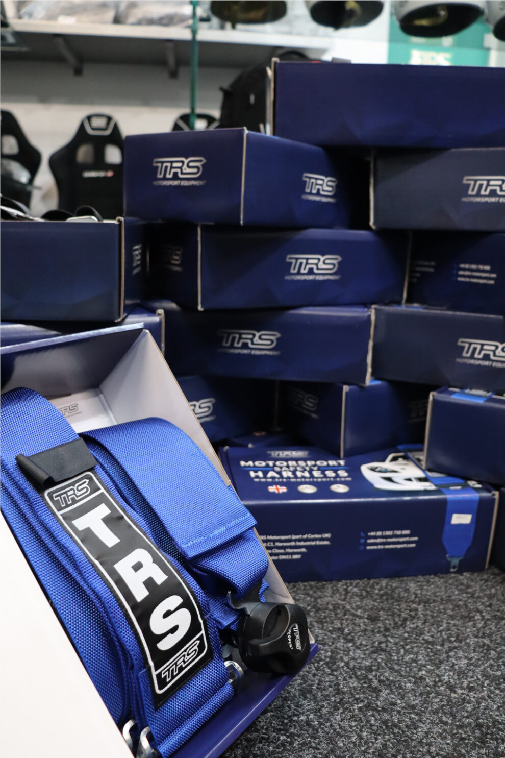 A blue TRS harness in its open box in front of a stack of blue TRS harness boxes in the GSM Performance showroom