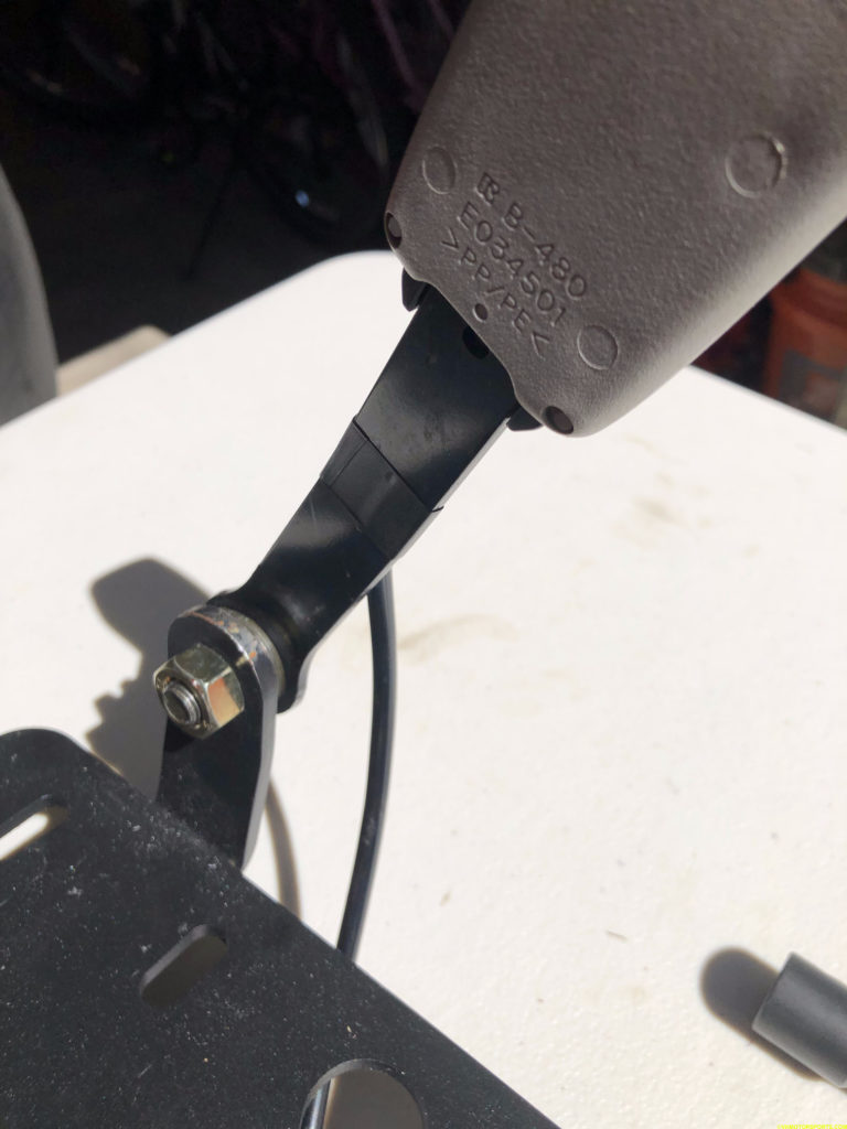 Original seat belt buckle stalk bolted to a black steel seat side bracket on the bench