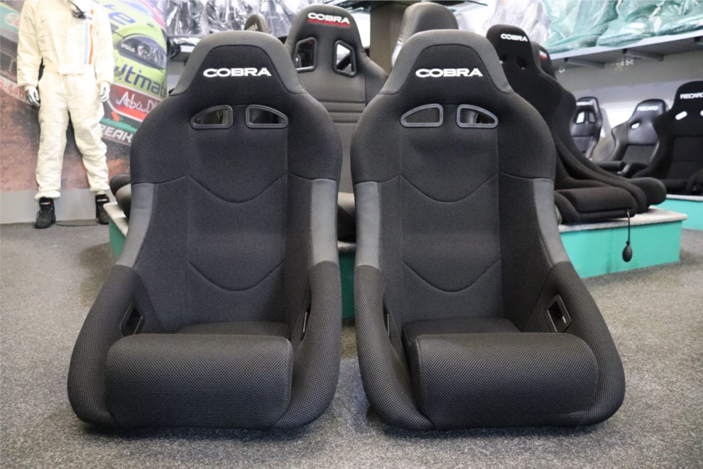 A pair of black Cobra Clubman bucket seats in 3D spacer fabric on the showroom floor, with more Cobra and Recaro seats on the display behind