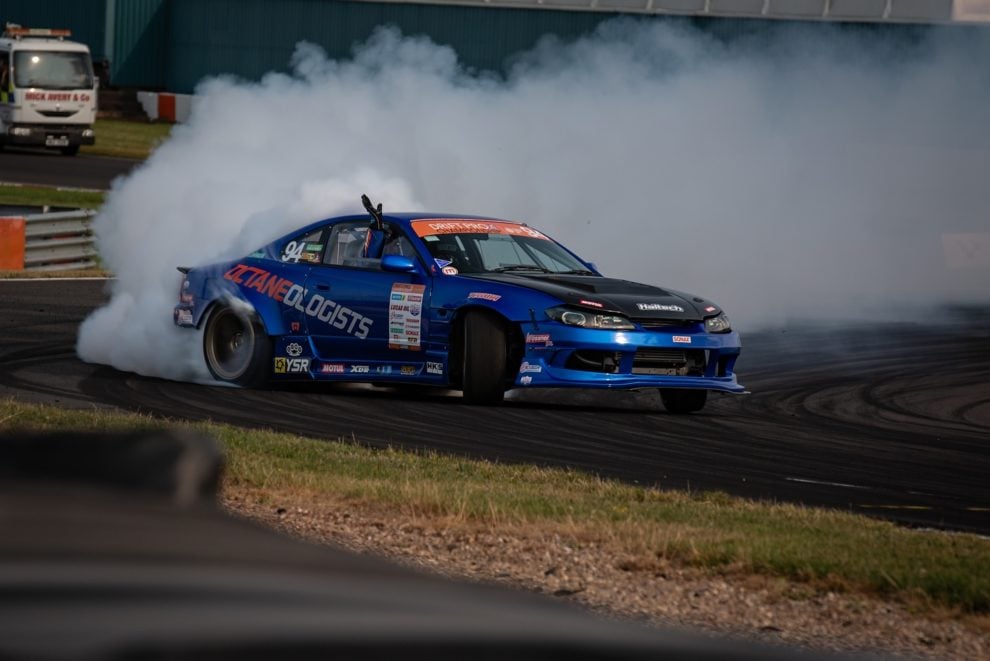 A blue Nissan Silvia drift car sliding sideways in a cloud of tyre smoke at Donington Park