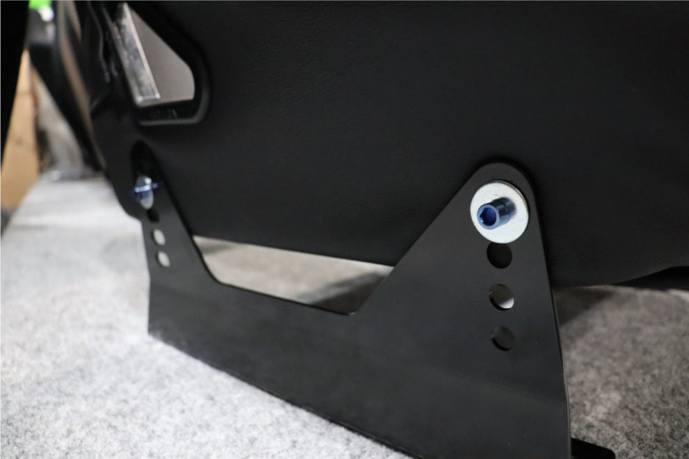 A blue titanium M8 bolt and washer fixing a black bucket seat to a black steel side mount bracket