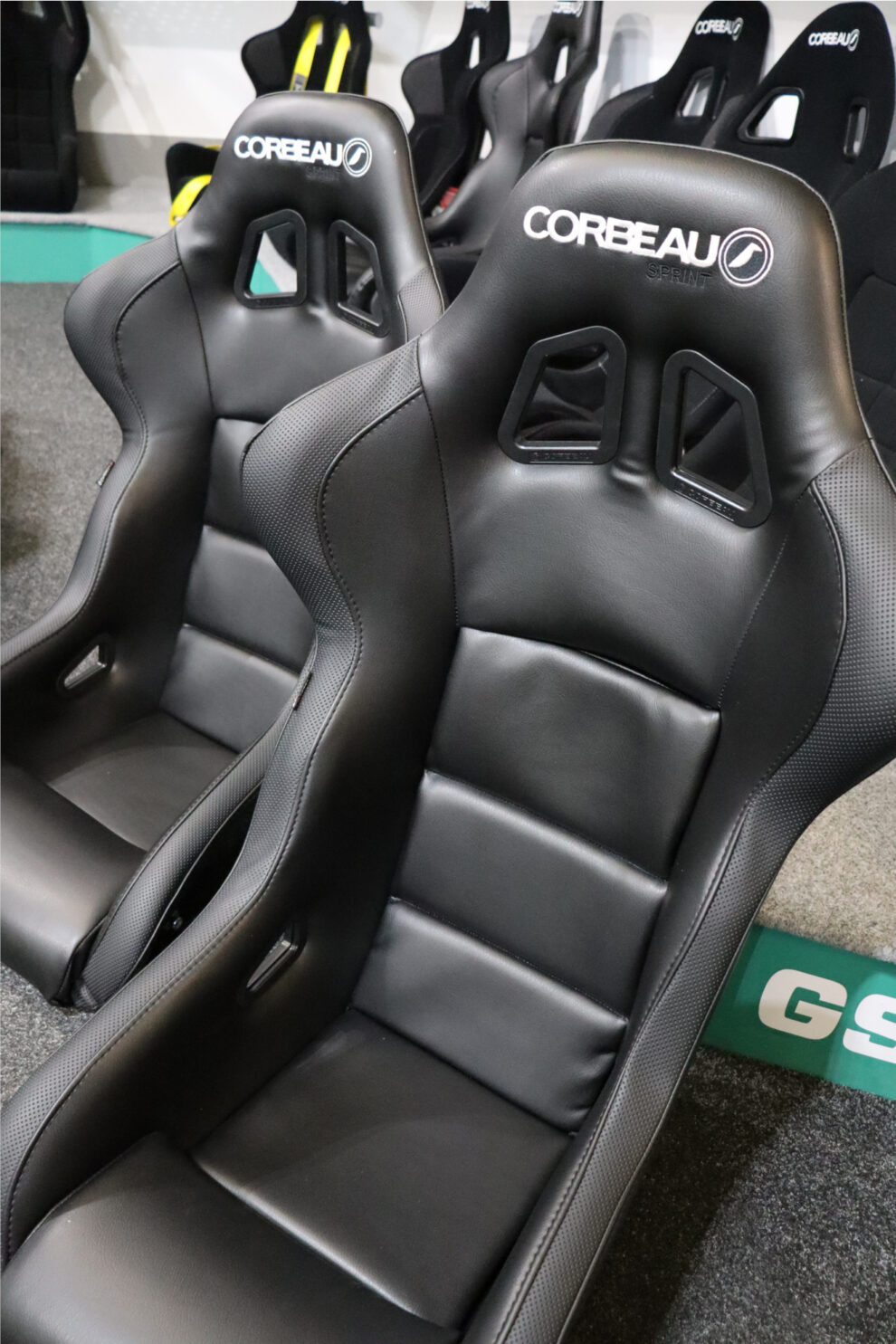 A black vinyl Corbeau Sprint seat with the Sprint name under the Corbeau logo, with the second seat of the pair behind