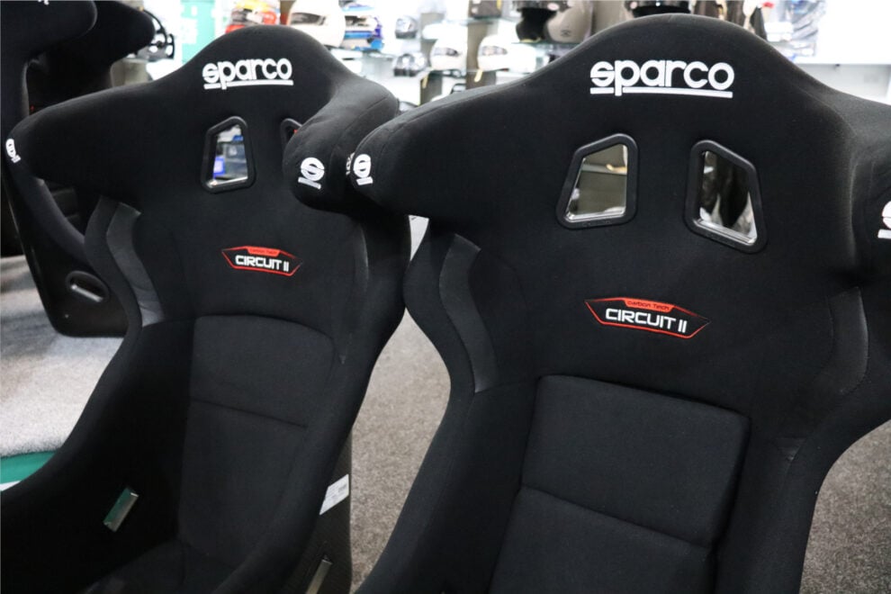 A pair of black Sparco Circuit II bucket seats with head wings and Circuit II badges in the GSM Performance showroom, with helmets on the shelves behind
