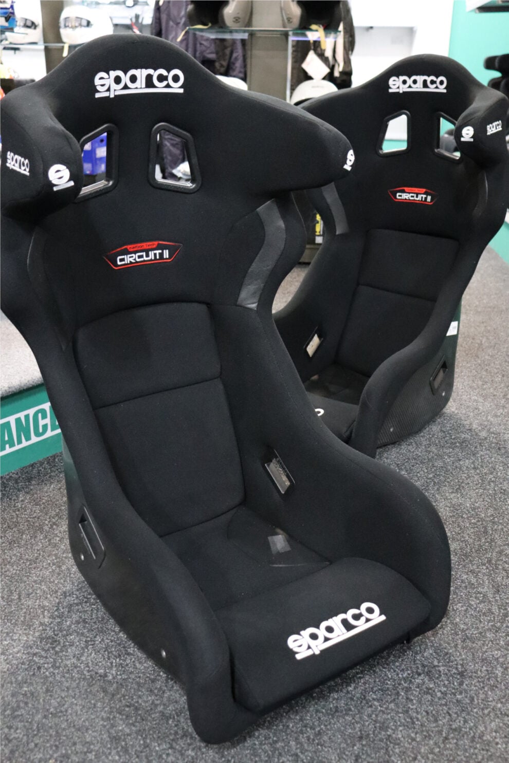A black Sparco Circuit II seat seen from the front on the showroom floor, with a second one behind showing its carbon fibre shell