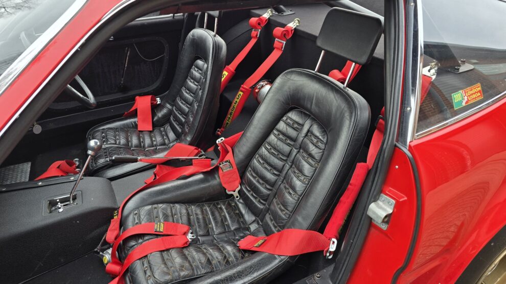 The original black leather seats in a Ferrari Daytona, with red harnesses and a roll bar behind them