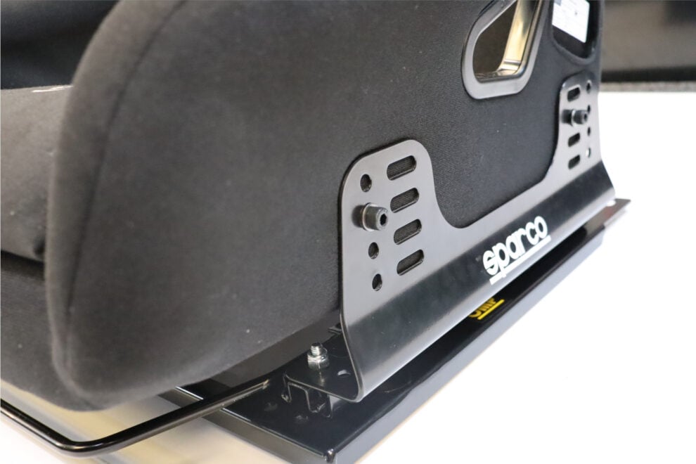 An OMP TRS-E XL seat bolted to black Sparco side mounts, sitting on runners with a lever, on a base plate