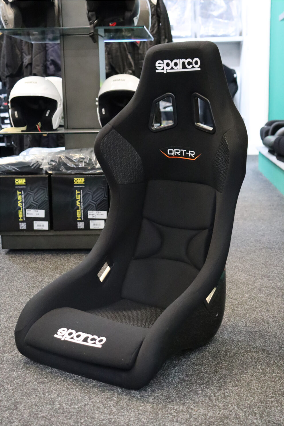 A black Sparco QRT-R sim racing seat standing in the showroom in front of OMP helmet boxes