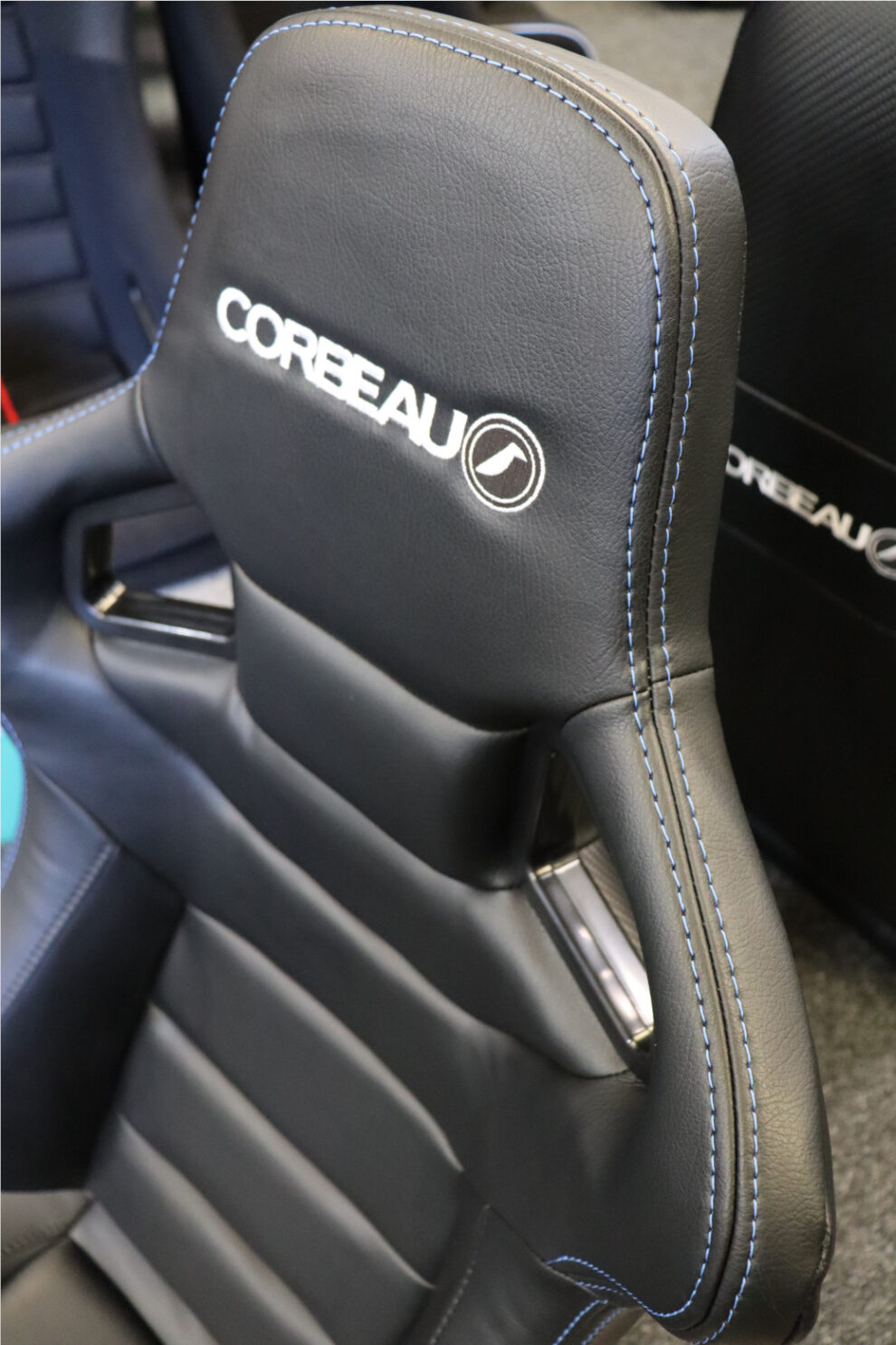 Close up of the headrest of a black Corbeau RRS seat with blue stitching along the seams and the Corbeau logo