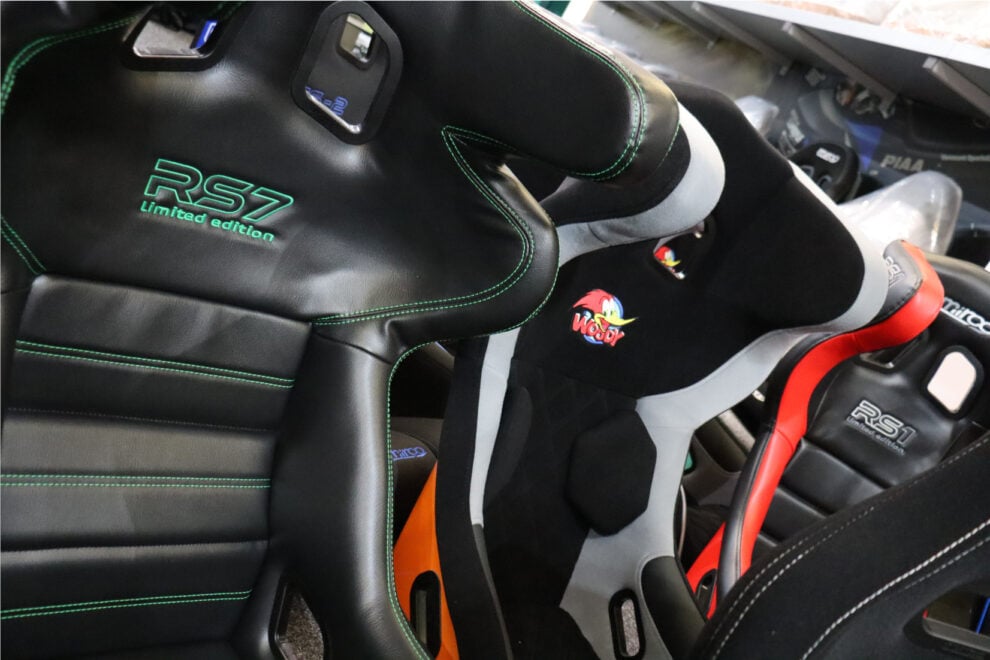 Close view of a black vinyl Mirco RS7 Limited Edition with green stitching and embroidery, beside other customer-specified Mirco seats