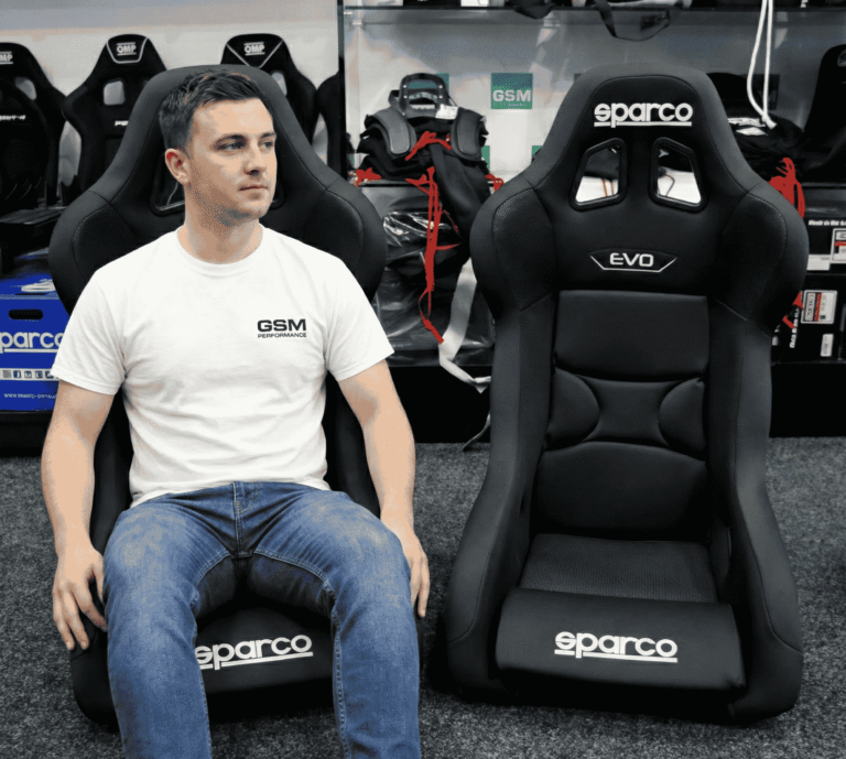 A GSM team member sitting next to a black Sparco Evo bucket seat in our showroom to show the size