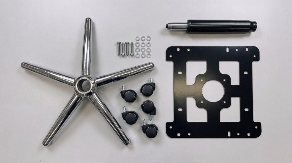 Overhead view of the parts of an office chair conversion kit laid out on a bench: a chrome five arm star, castors, a black gas lift column, bolts and a laser cut steel adaptor plate with slots and round holes around its edges