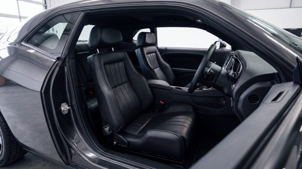 Looking into the cabin of a modern American muscle car coupe through the open driver door, both front seats replaced with matching black leather retro reclining sport seats