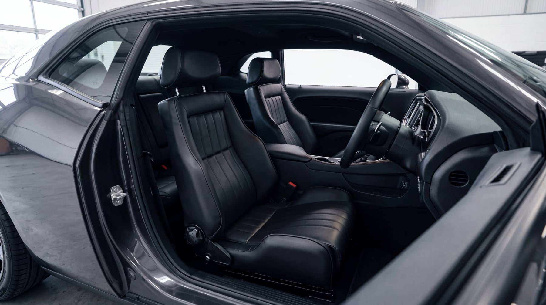 Looking into the cabin of a modern American muscle car coupe through the open driver door, both front seats replaced with matching black leather retro reclining sport seats