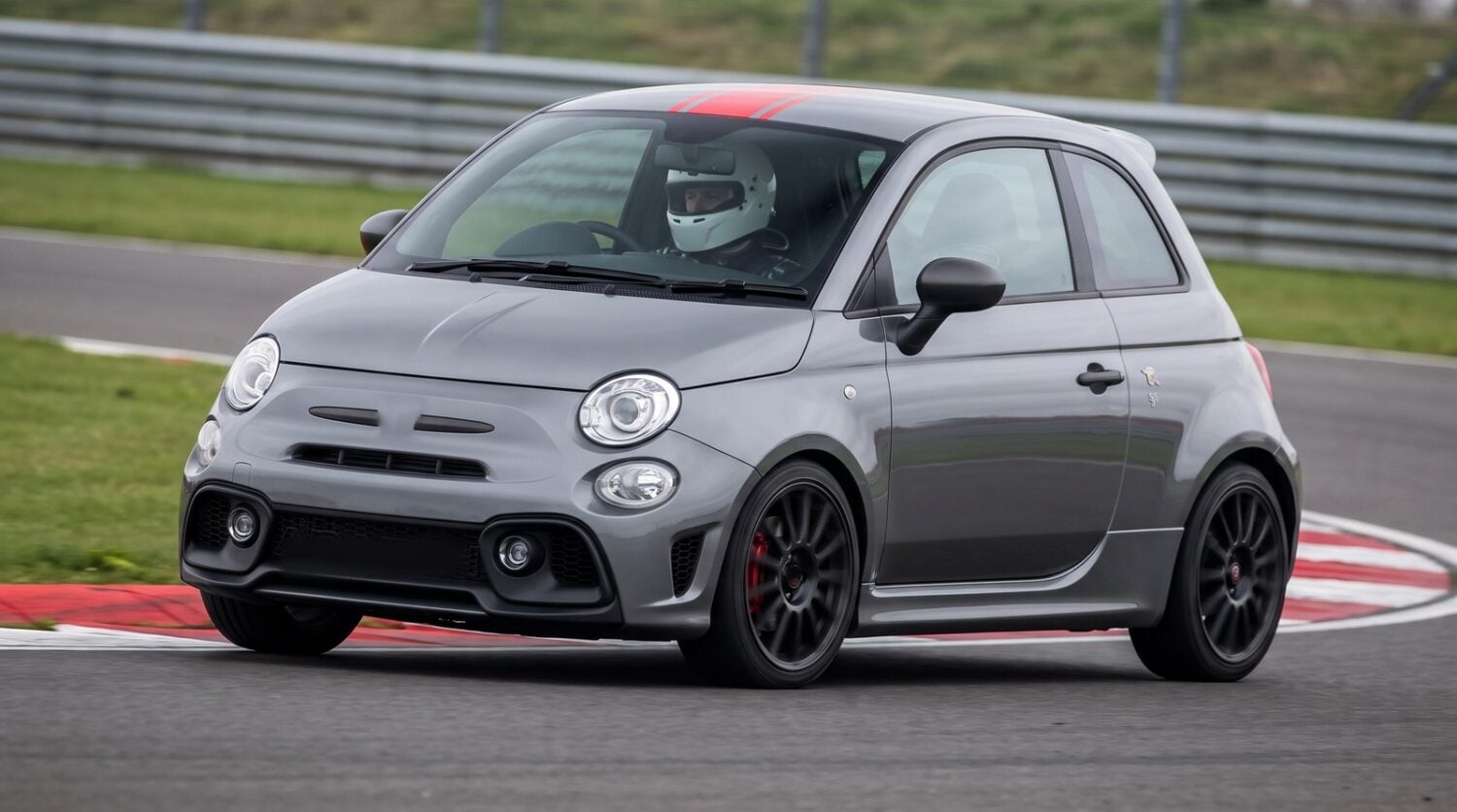 Grey Abarth 595 with a red roof stripe cornering at an apex on a British race circuit with a helmeted driver at the wheel
