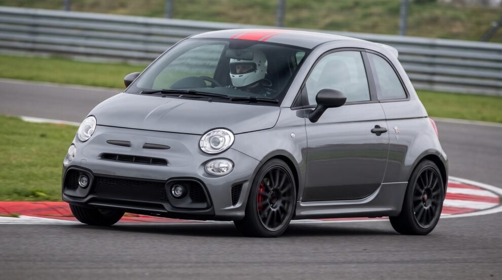 Grey Abarth 595 with a red roof stripe cornering at an apex on a British race circuit with a helmeted driver at the wheel