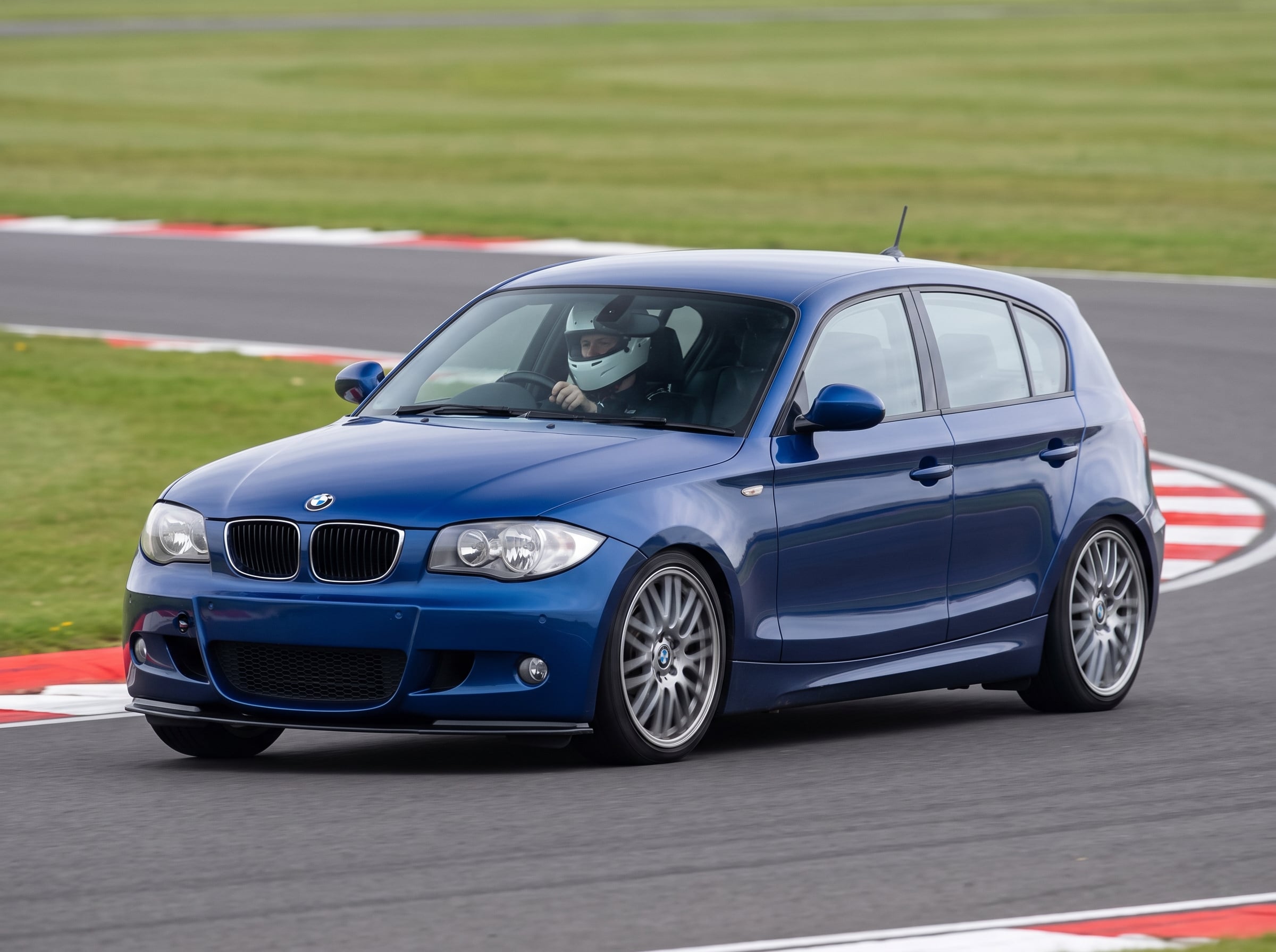 Le Mans Blue BMW 1 Series E87 on a British race circuit at an apex with red and white kerbing