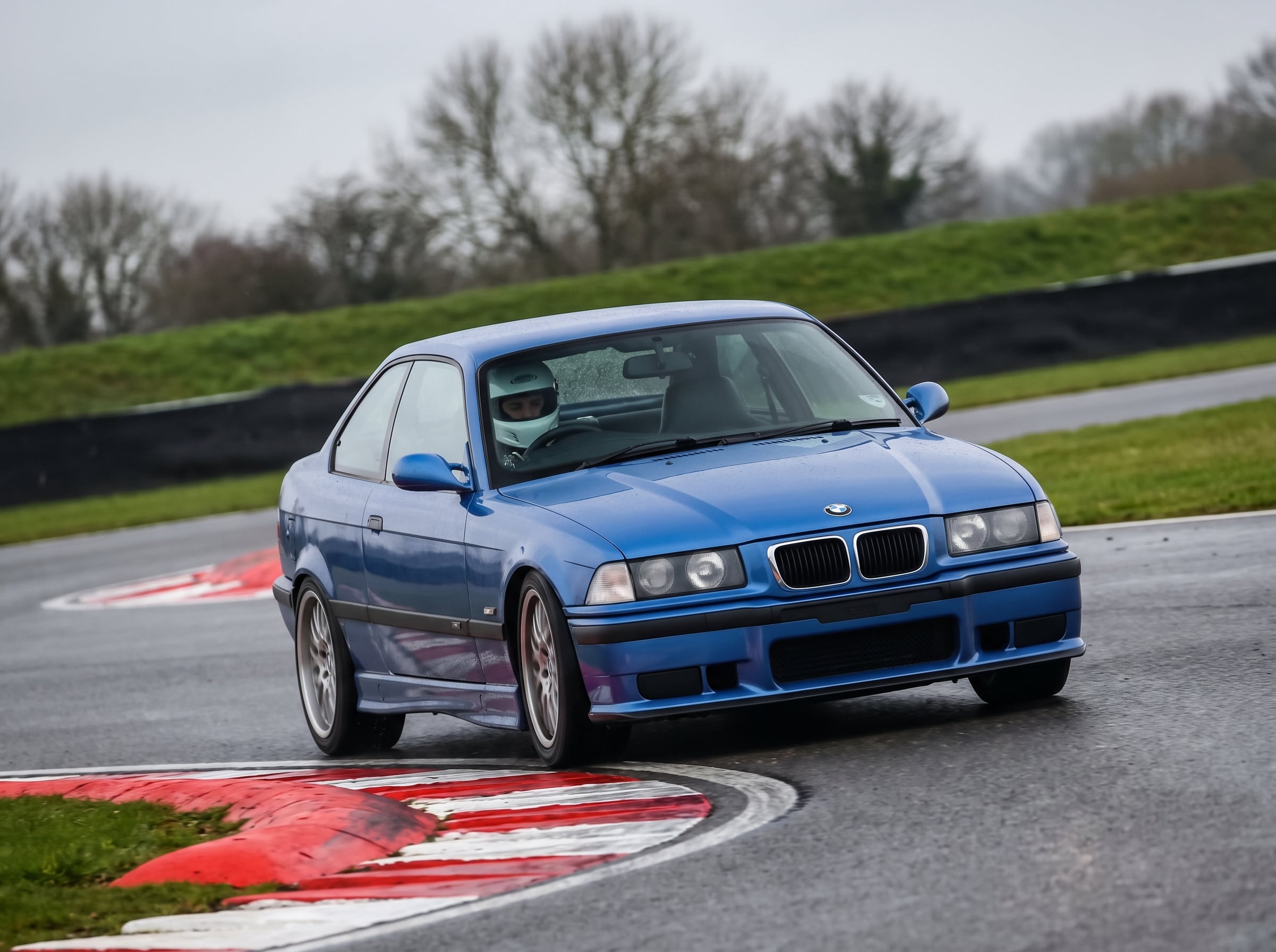 Estoril Blue BMW 3 Series E36 on a British race circuit at an apex with red and white kerbing