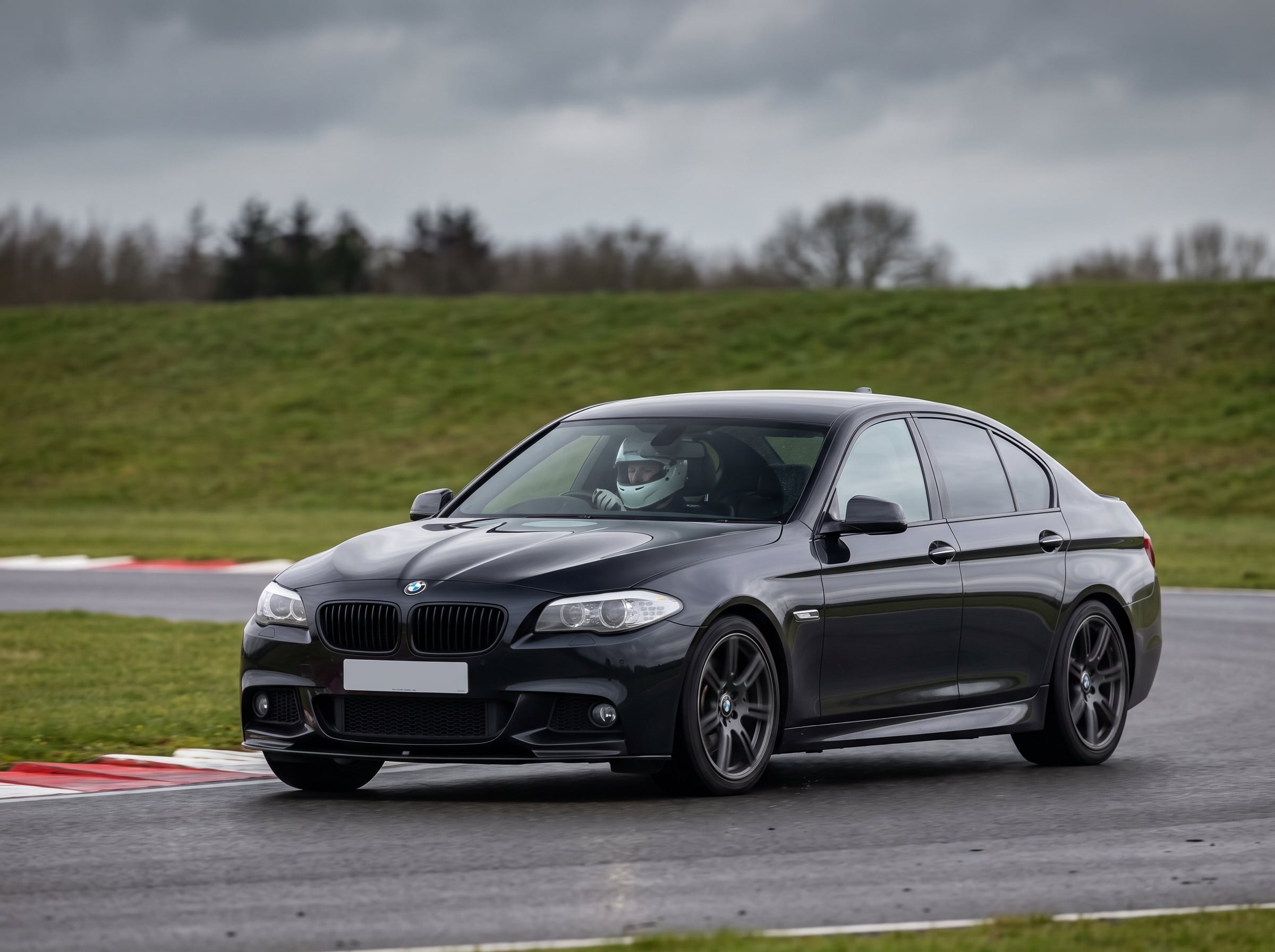 Carbon Black BMW 5 Series F10 on a British race circuit at an apex with red and white kerbing