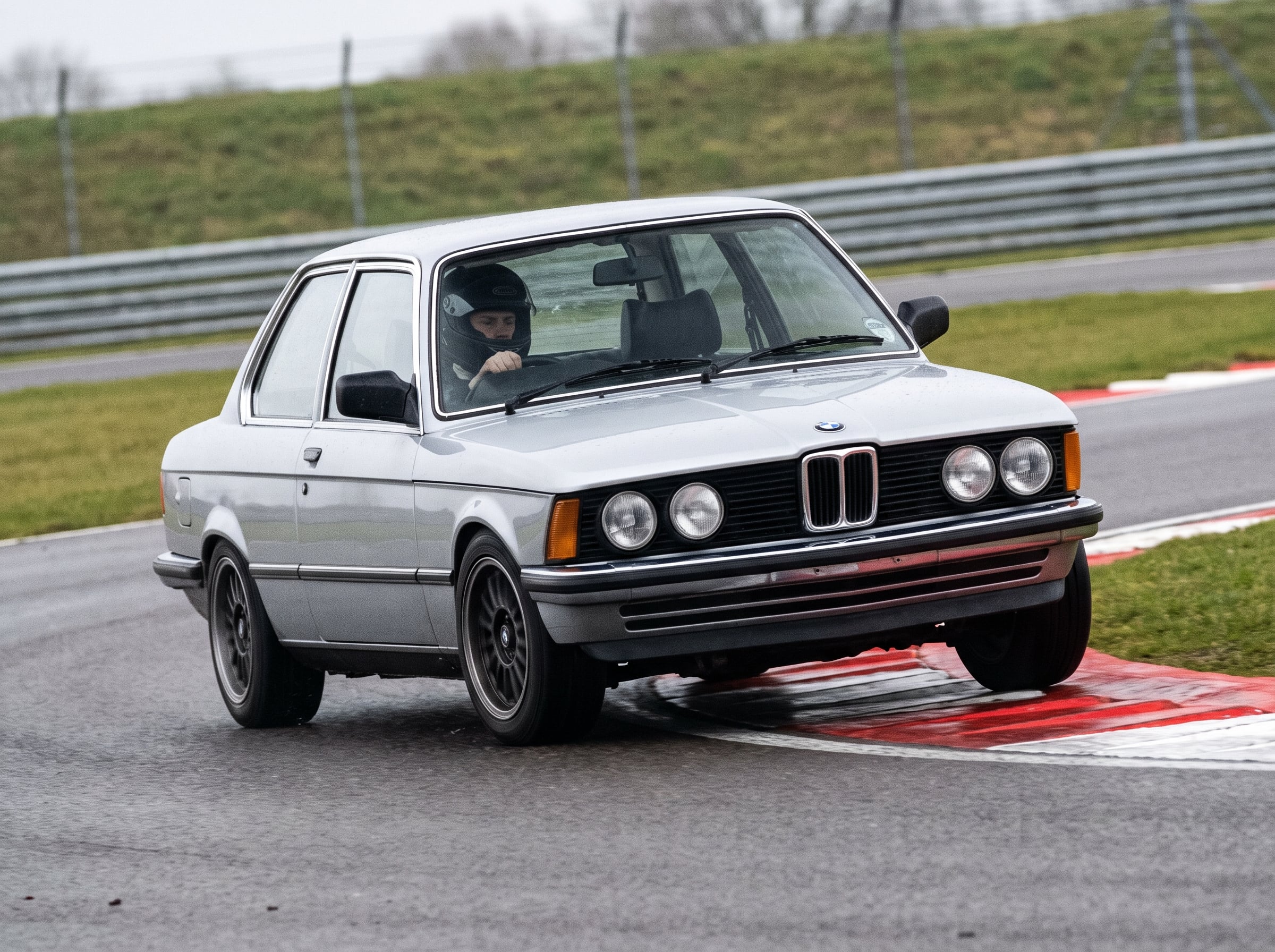 Polaris Silver BMW 3 Series E21 on a British race circuit at an apex with red and white kerbing