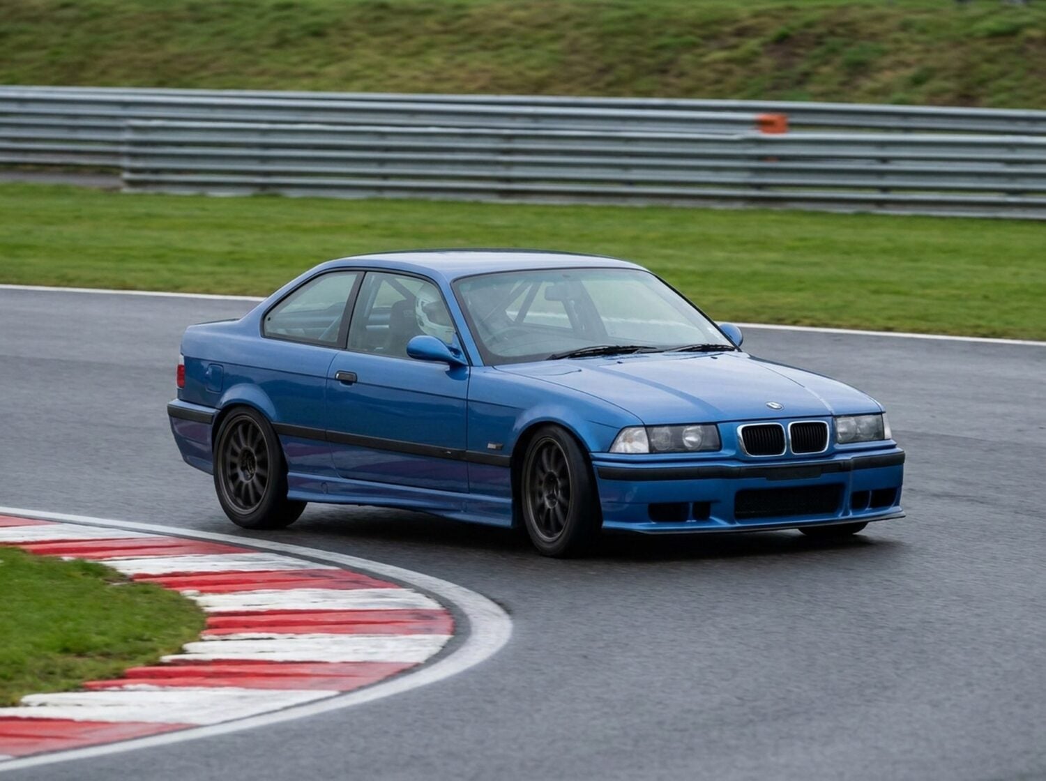 BMW E36 M3 cornering on a British race circuit with a roll cage visible through the side glass