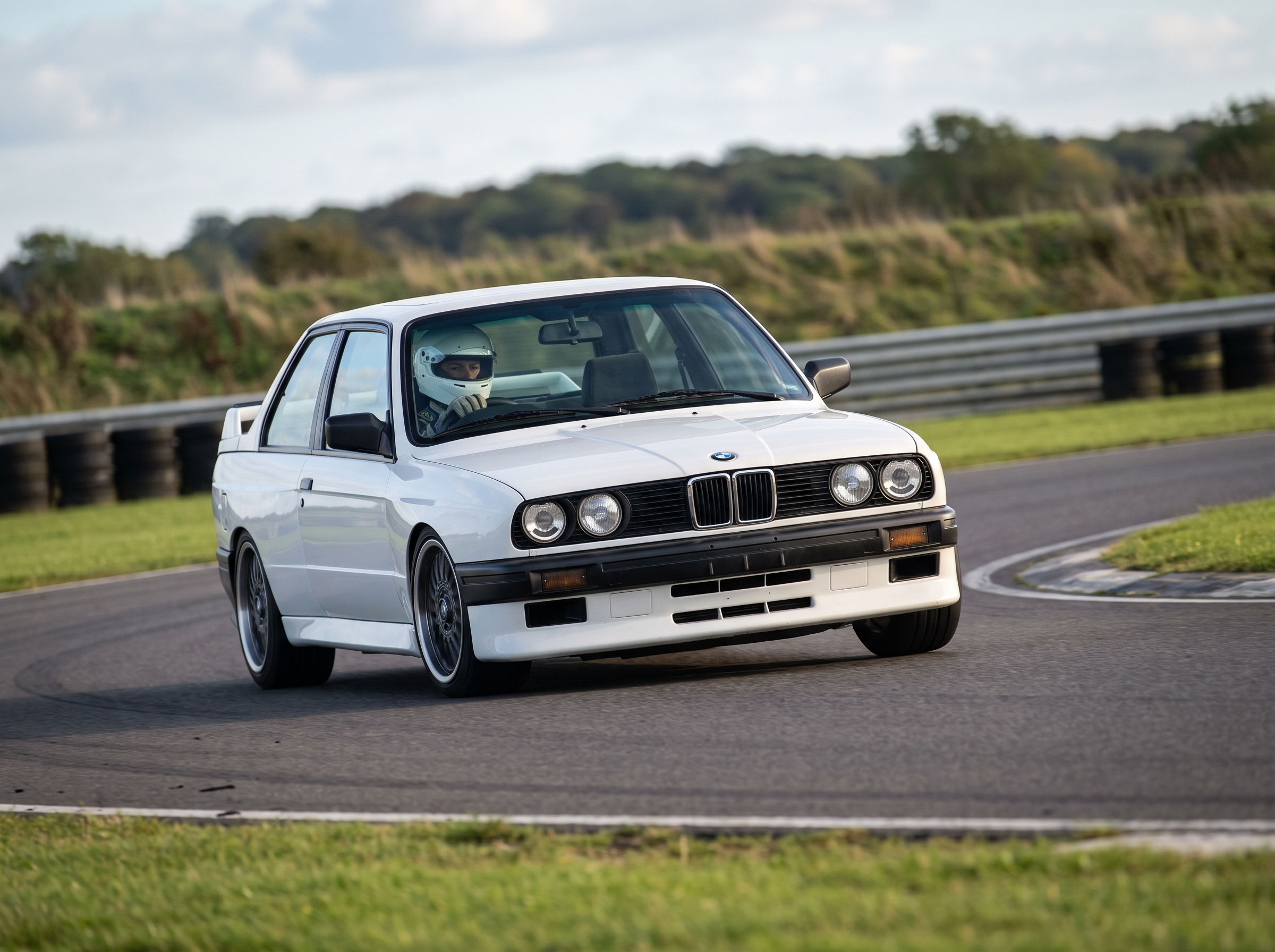 White BMW M3 E30 cornering on a British race circuit, helmeted driver at the wheel