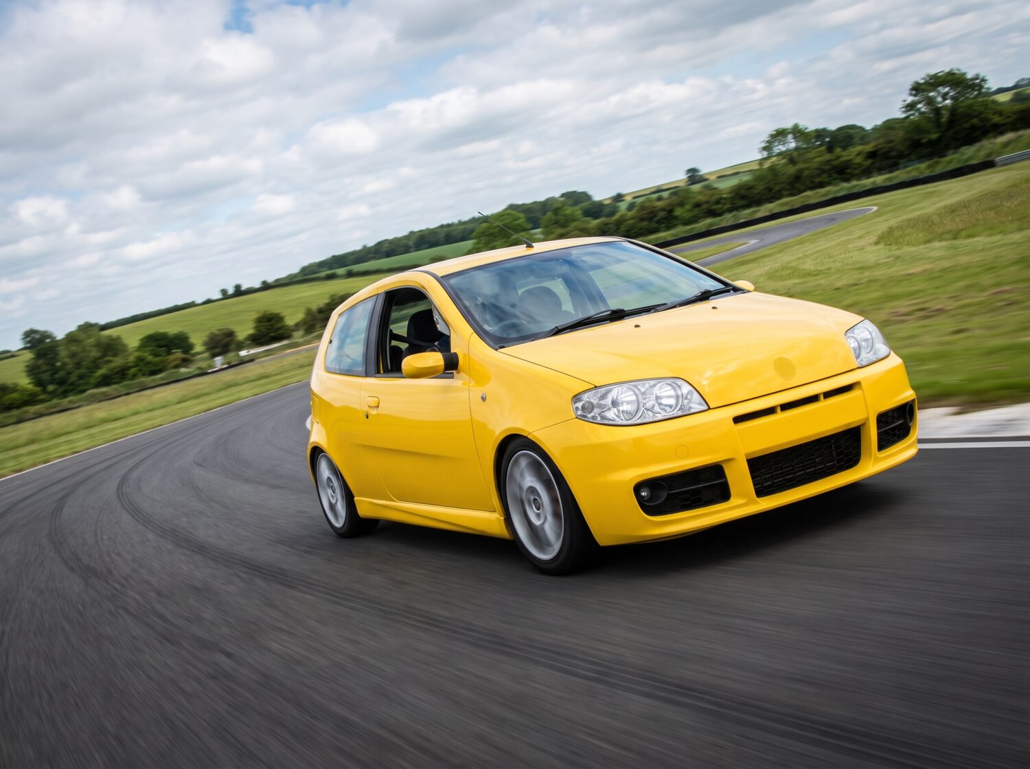 Yellow Fiat Punto Mk2 accelerating out of a corner at a British club circuit