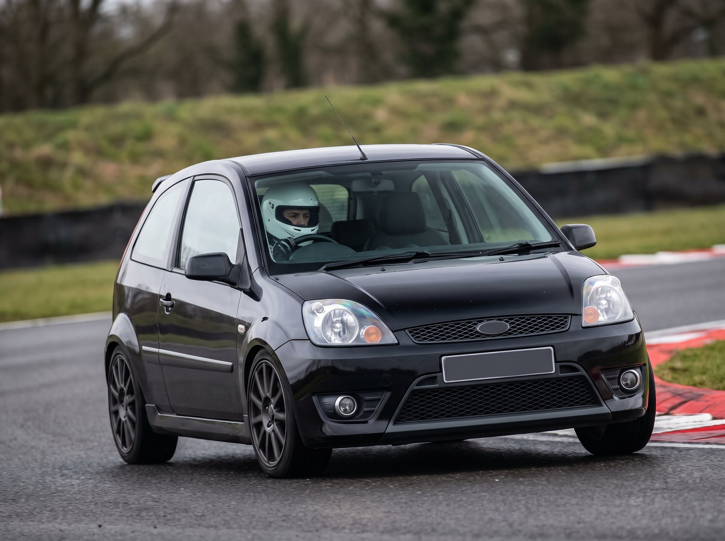 Black Ford Fiesta ST150 Mk5 on a British race circuit at an apex with red and white kerbing