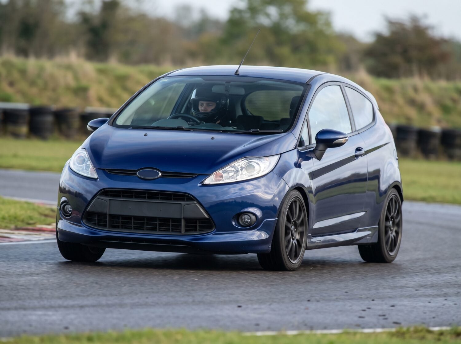 Midnight blue Ford Fiesta Mk6 hatchback cornering on a British club racing circuit