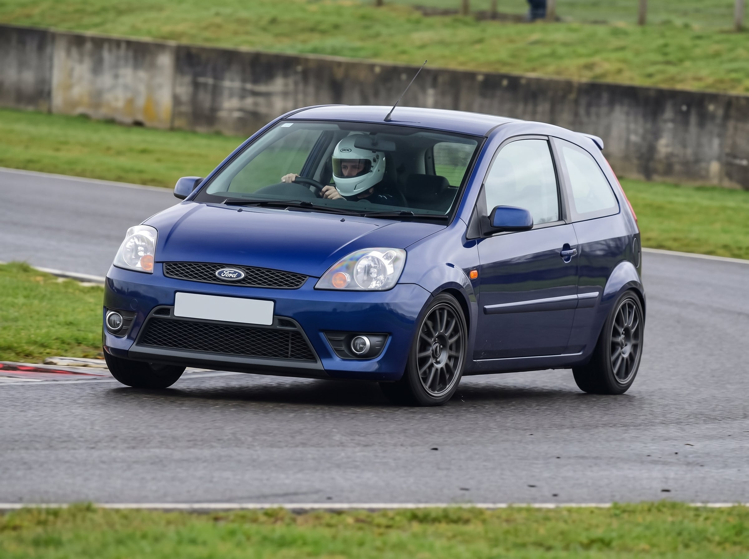 Midnight blue Ford Fiesta Mk6 hatchback cornering on a British club racing circuit