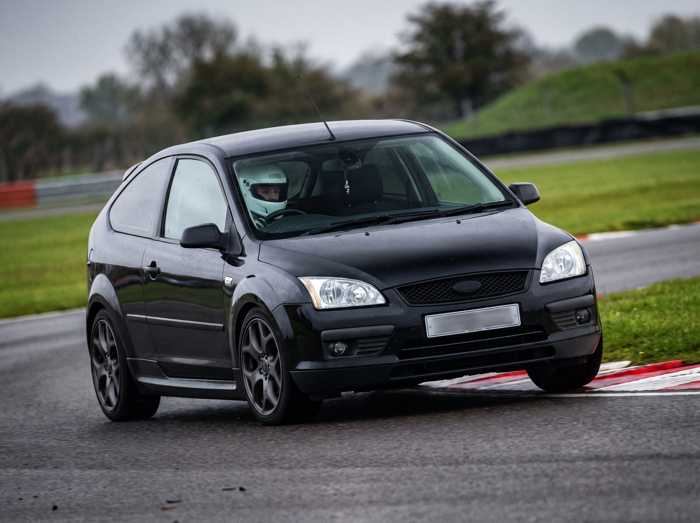 Black Ford Focus Mk2 on a British race circuit at an apex with red and white kerbing