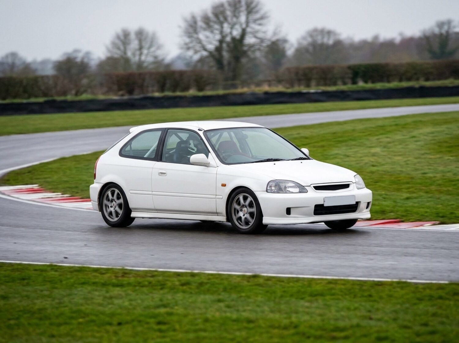 White Honda Civic EK9 Type R cornering on a British race circuit with a bucket seat visible through the side glass