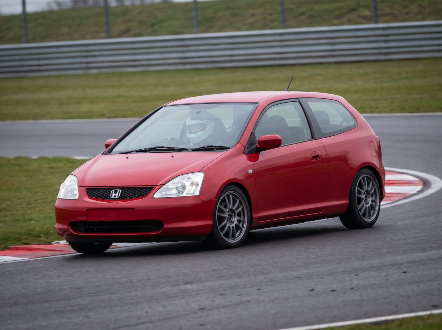Milano Red Honda Civic EP2 on a British race circuit at an apex with red and white kerbing