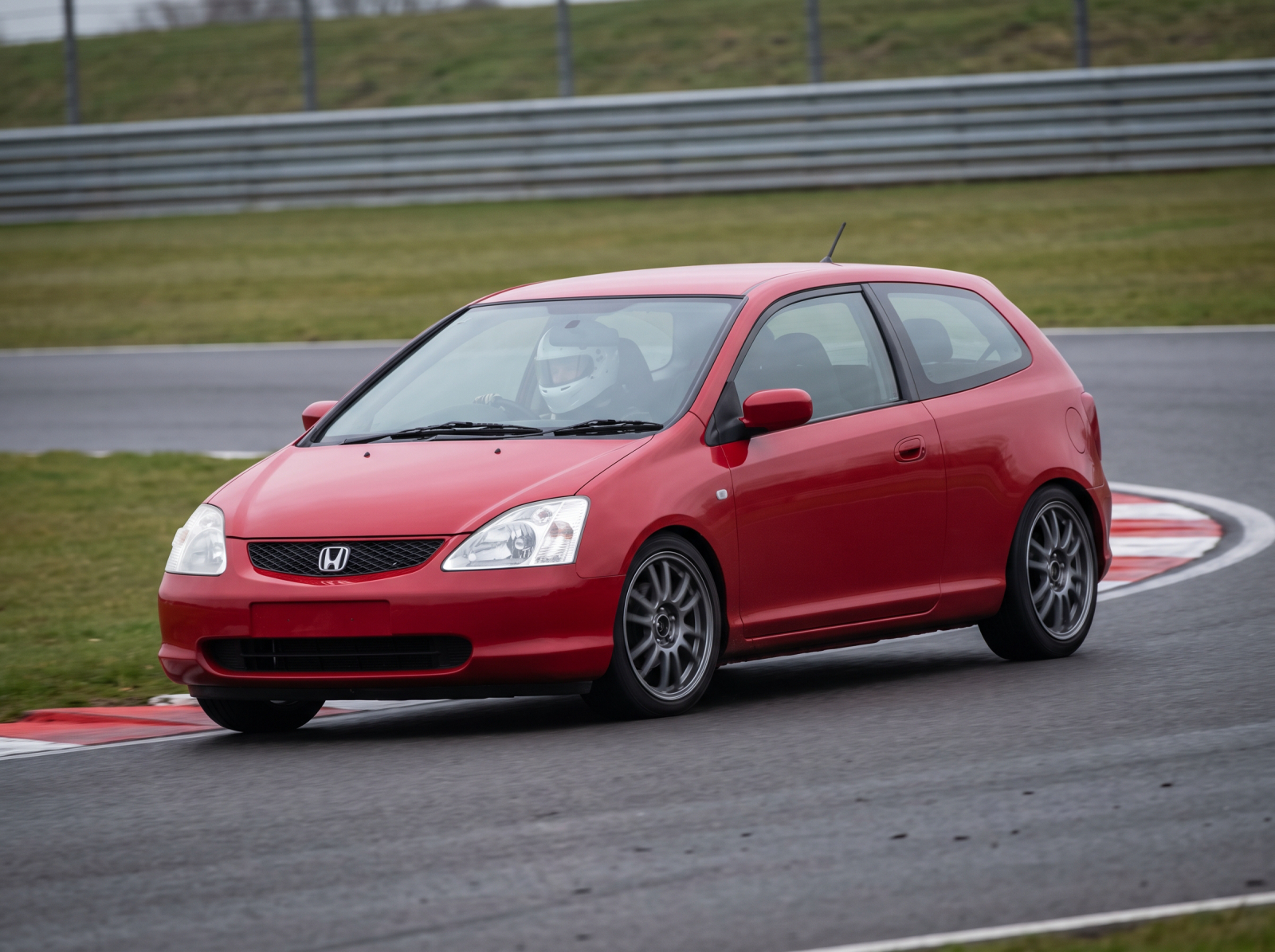 Milano Red Honda Civic EP2 on a British race circuit at an apex with red and white kerbing