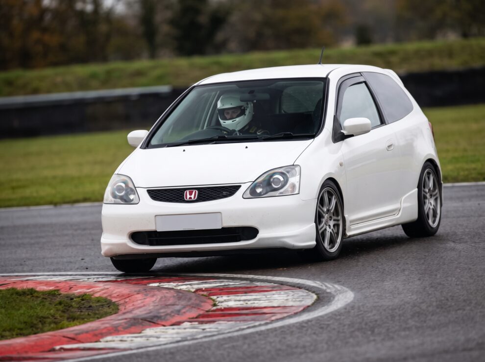 A white Honda Civic Type R EP3 cornering over red and white kerbs on a race circuit