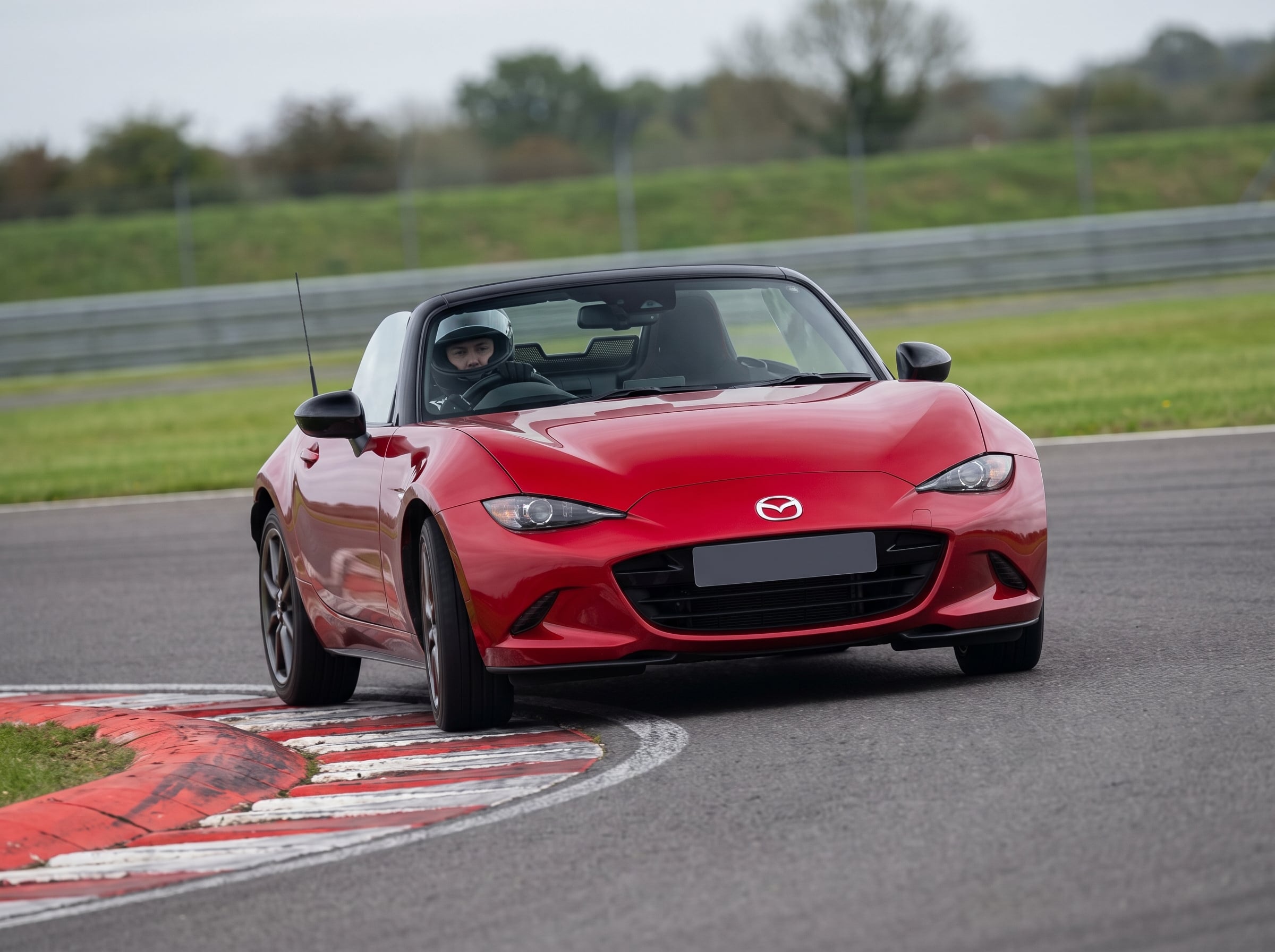 Red Mazda MX-5 Mk4 ND roadster on a British race circuit at an apex with red and white kerbing