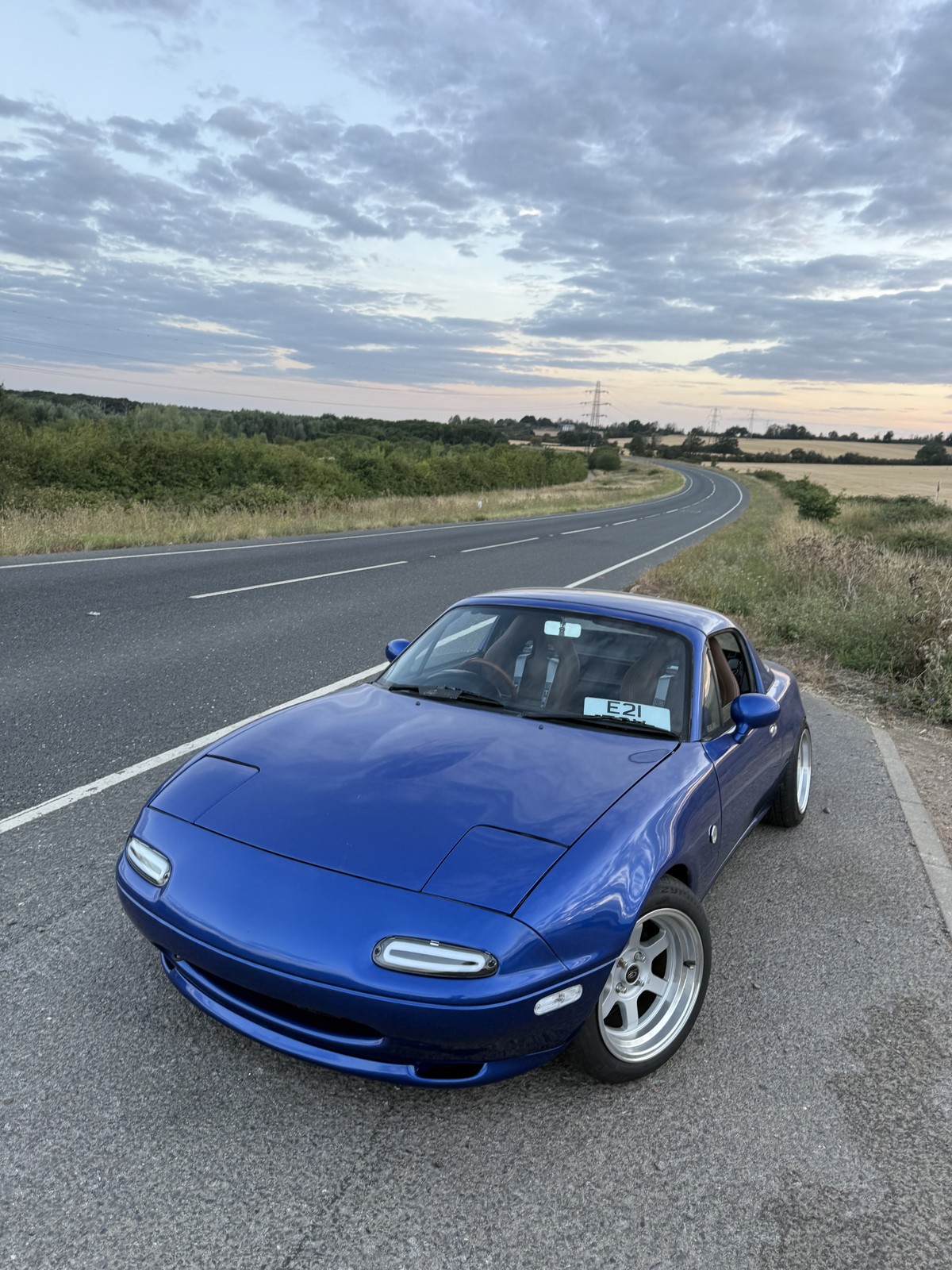 Blue Mk1 Mazda MX-5 on a country road at sunset after a full rebuild