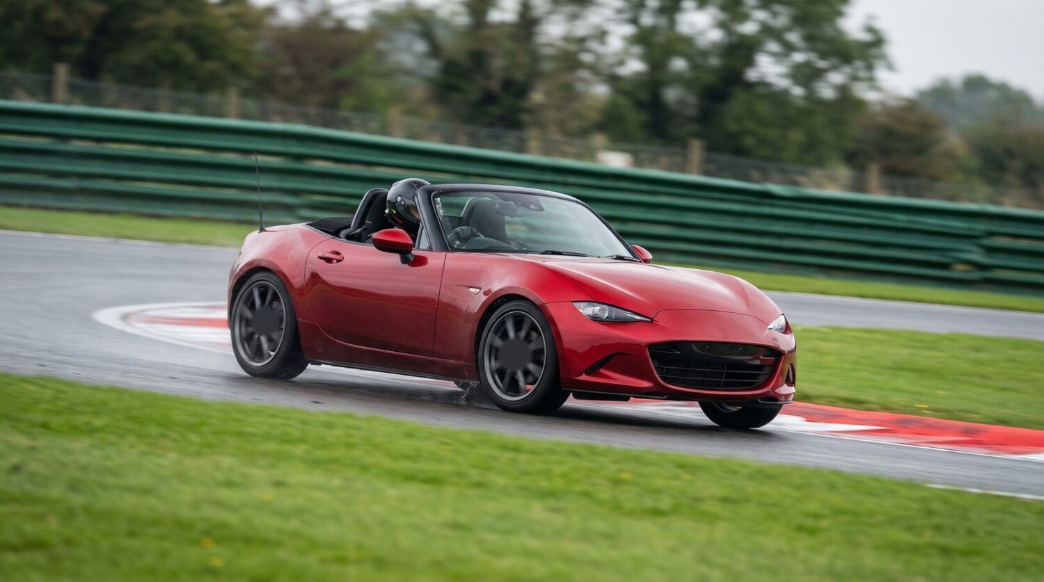 Red Mazda MX-5 Mk4 ND roadster cornering at an apex on a British race circuit with the roof down