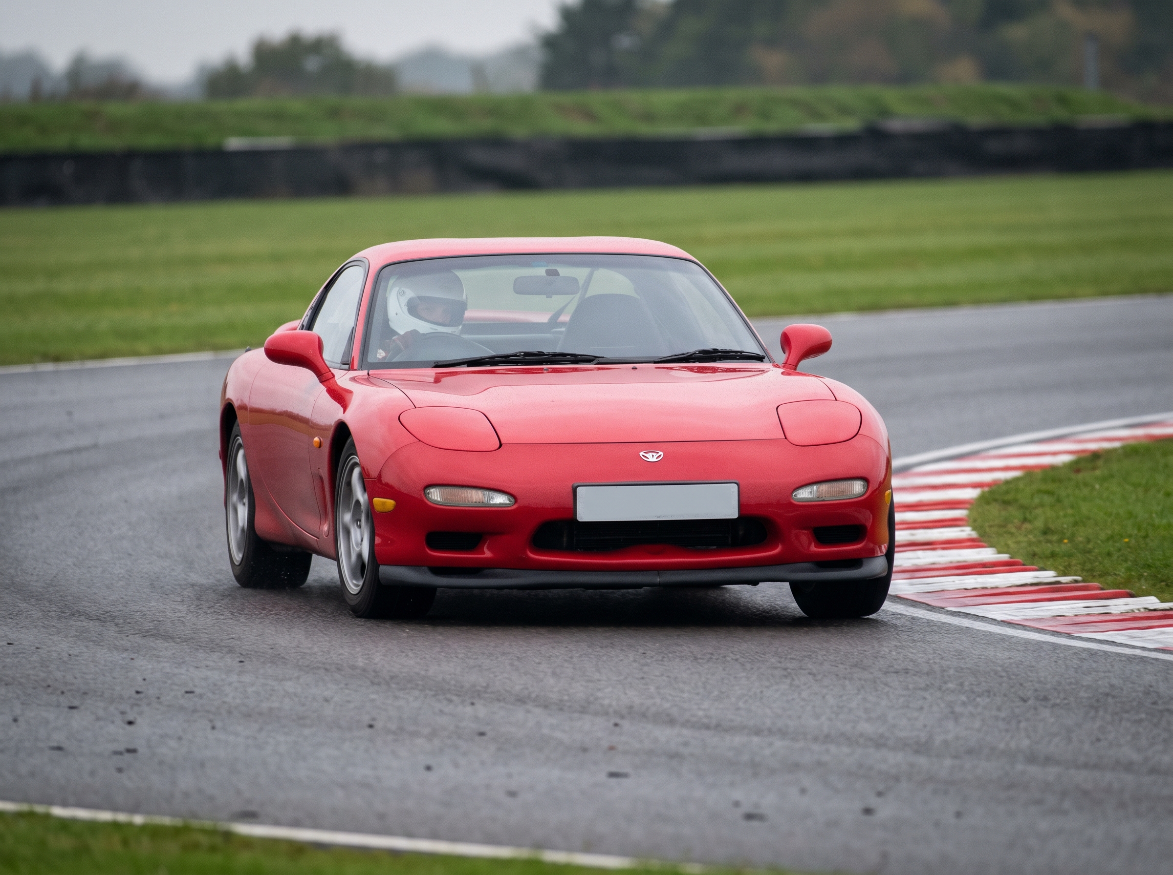 Red Mazda RX-7 third generation FD coupe on a British race circuit at an apex with red and white kerbing